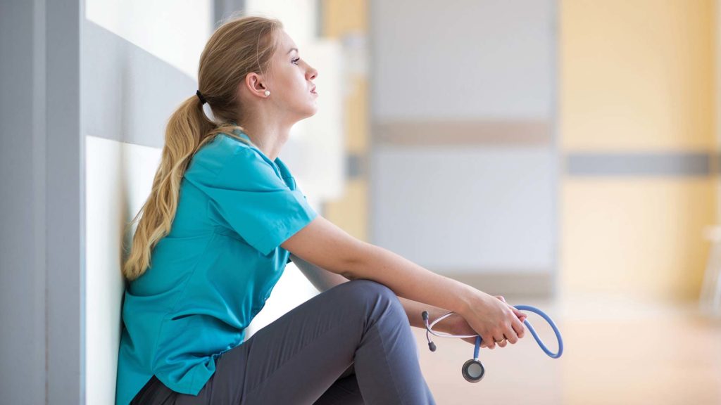 Exhausted nurse leaning against wall in hospital